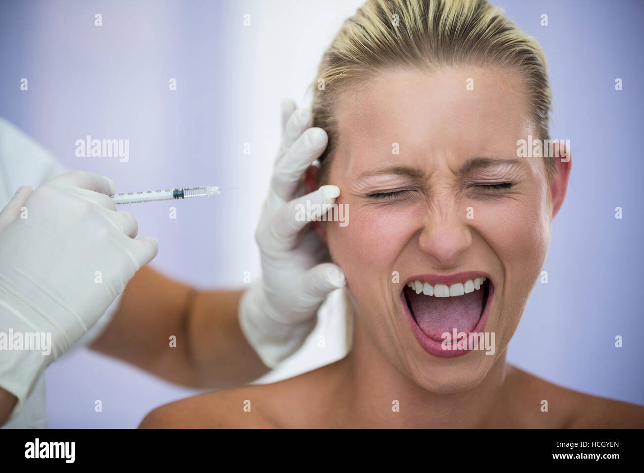 Asustada mujer gritando mientras recibe una inyección de tratamiento cosmético Foto de stock