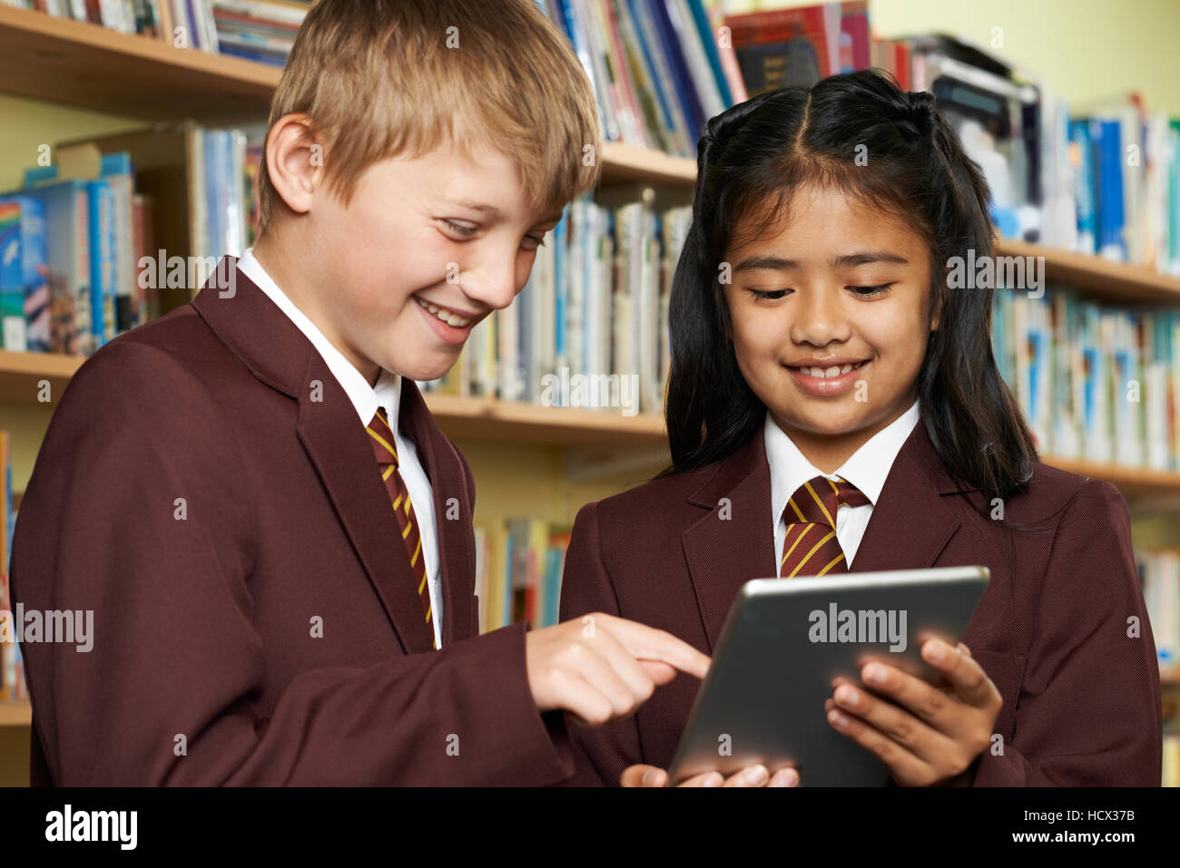 Los alumnos vistiendo uniforme escolar utilizando Tablet Digital en la biblioteca Foto de stock