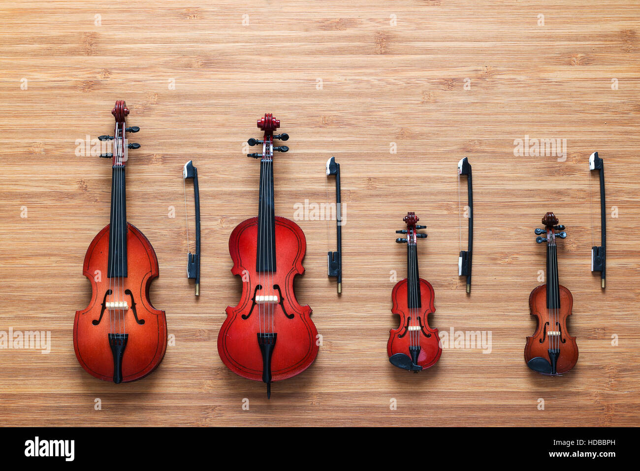 Conjunto de cuatro instrumentos de orquesta musical cadena de juguete:  violín, violonchelo, contrabajo, viola, sobre un fondo de madera. Cuarteto.  Concepto de música Fotografía de stock - Alamy