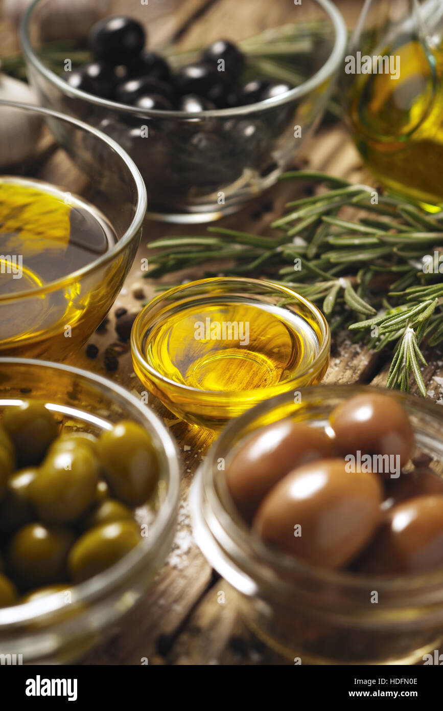 El aceite de oliva con aceitunas y romero en la vertical de la mesa de madera Foto de stock