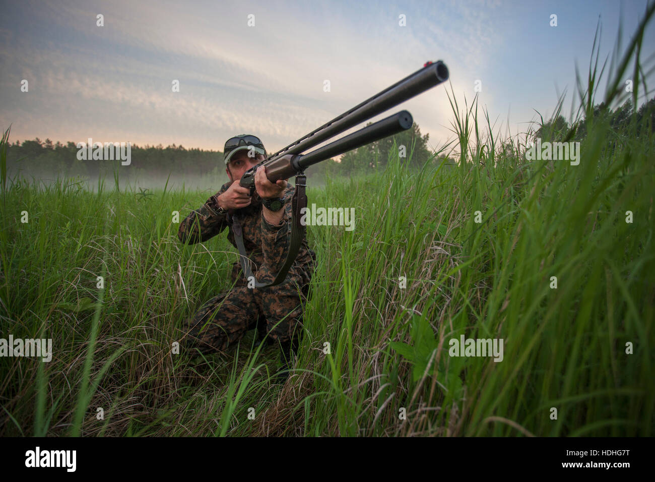 Cazador apuntando rifle mientras arrodillados en campo contra el cielo Foto de stock