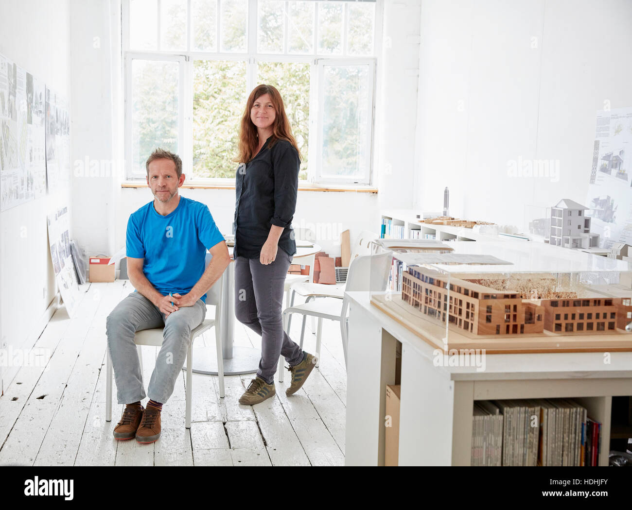 Una oficina moderna con paredes blancas y pisos. Un hombre sentado y una mujer de pie. Un modelo de arquitectura en una tabla. Foto de stock