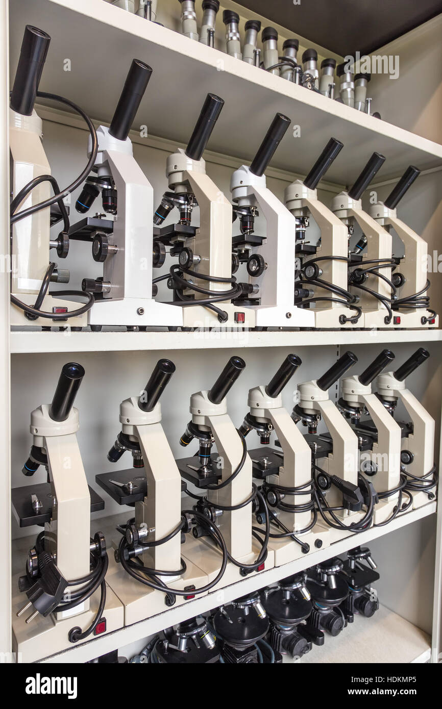 Armario con filas de microscopios en estantes en la escuela secundaria Foto de stock