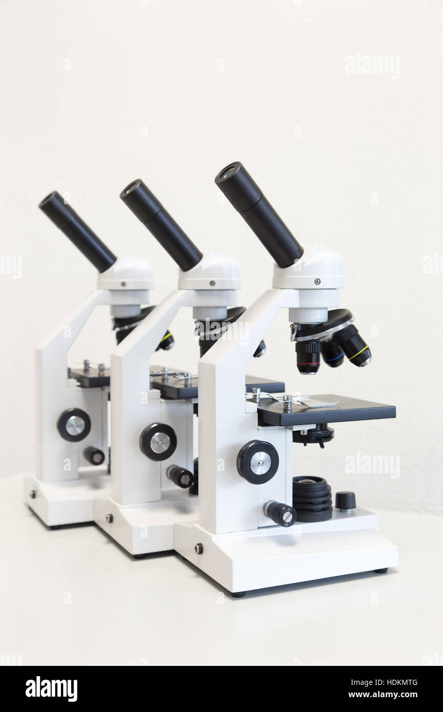 Tres estudiantes microscopios en una fila sobre antecedentes aislados Foto de stock