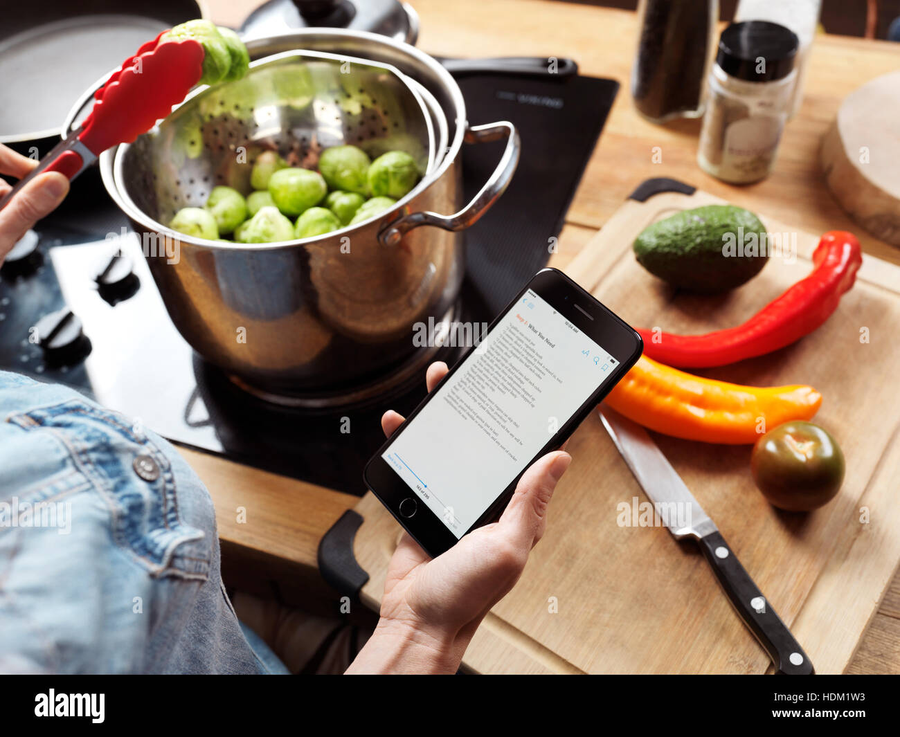 Mujer cocina en la cocina leyendo una receta desde el iPhone 7 en su mano Foto de stock