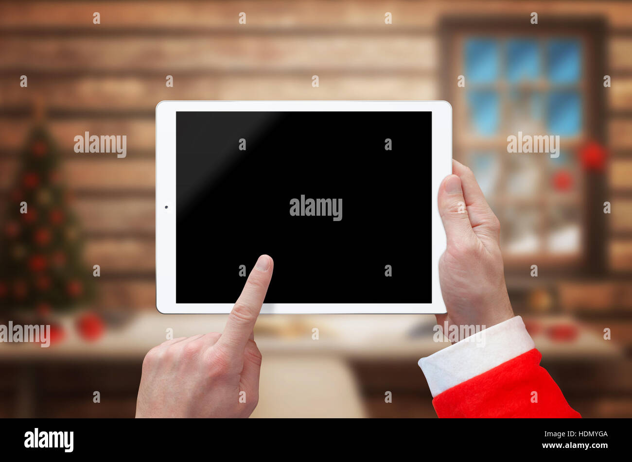 Tablet en Santa Claus mano con pantalla en blanco para el boceto. Casa de Santa Claus con el árbol de Navidad en el fondo. Foto de stock