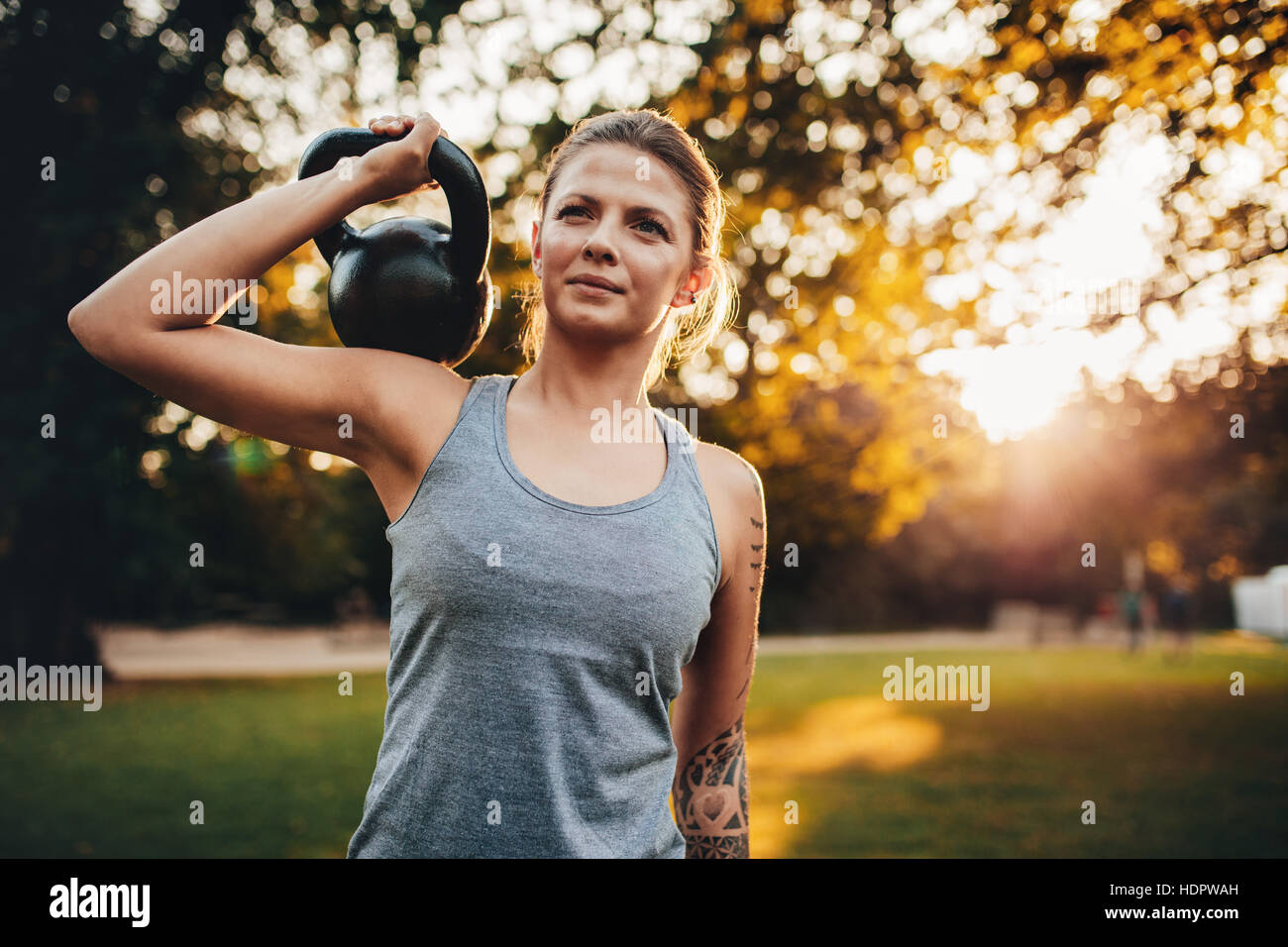 Colocar el retrato de mujer joven con kettlebell pesas en el parque. Mujer fitness entrenamiento con pesas en el parque. Foto de stock
