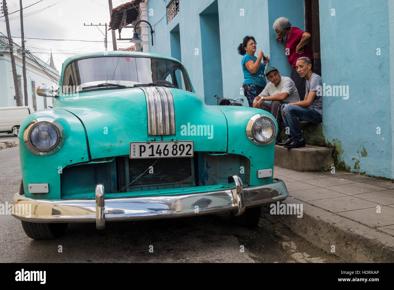 Sentado en la parte delantera el paso conversando junto a un viejo coche americano, Camagüey, Cuba Foto de stock