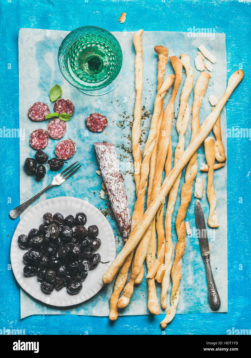 Grissini Bread Sticks, salchichas, aceitunas y vino blanco, fondo azul Foto de stock
