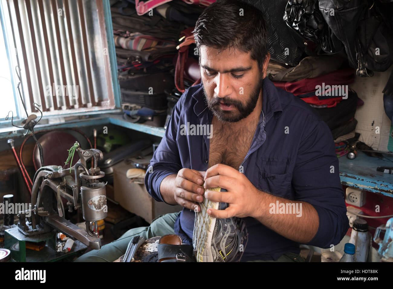 Un hombre repara zapatos en un stand en una acera en Yazd, la provincia de Yazd, Irán Foto de stock