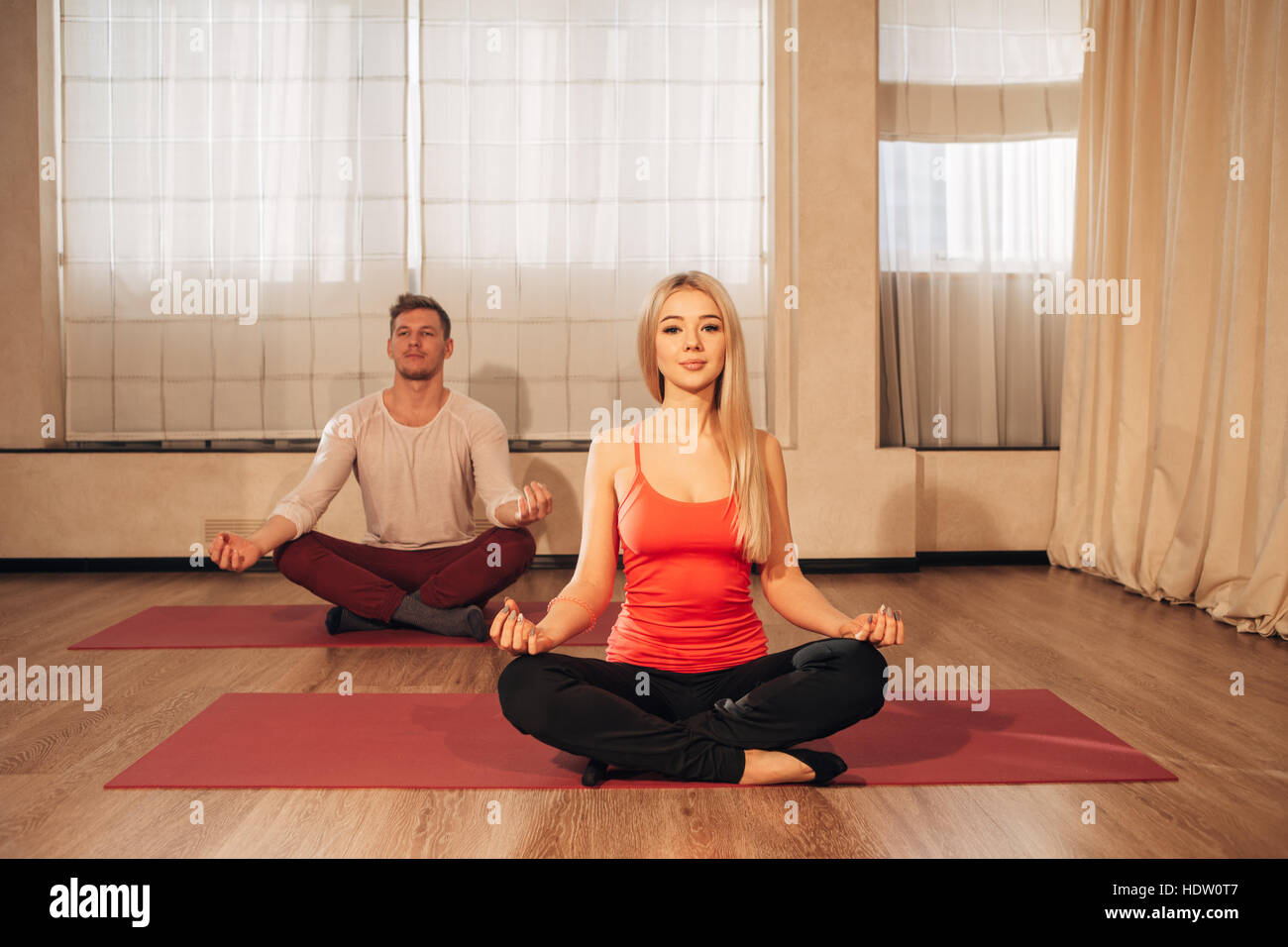 Hombre y mujer delgada sobre antecedentes meditando en pose de Lotus en el gimnasio Foto de stock