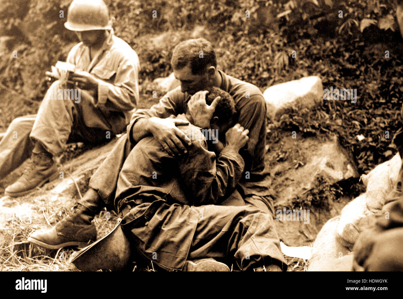 Un soldado de infantería estadounidense asolado por duelo cuyo compañero ha sido asesinado en acción es consolada por otro soldado. En el fondo un ayudante médico rellena metódicamente casualty etiquetas, Haktong-ni zona, Corea. El 28 de agosto de 1950. Foto de stock