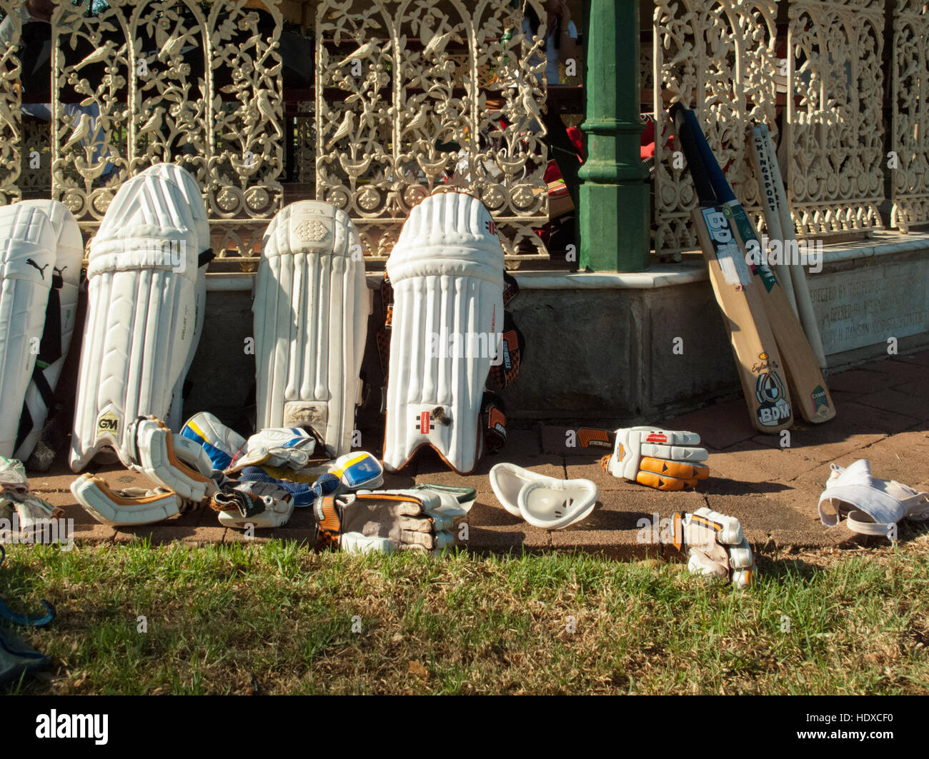 Guantes de cricket bat y almohadillas inclinándose hacia arriba contra la verja de hierro decorativo en la luz de la tarde Foto de stock