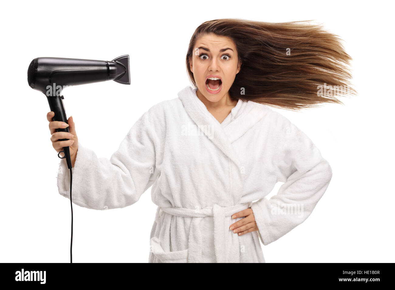 Conmocionó a la mujer en un albornoz secar su cabello con un secador de pelo aislado sobre fondo blanco. Foto de stock