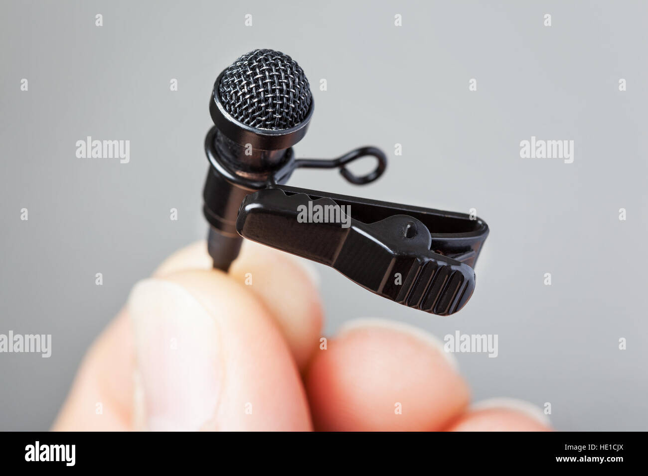 Close-up de una mano sujetando un micrófono clip de corbata con un fondo liso Foto de stock