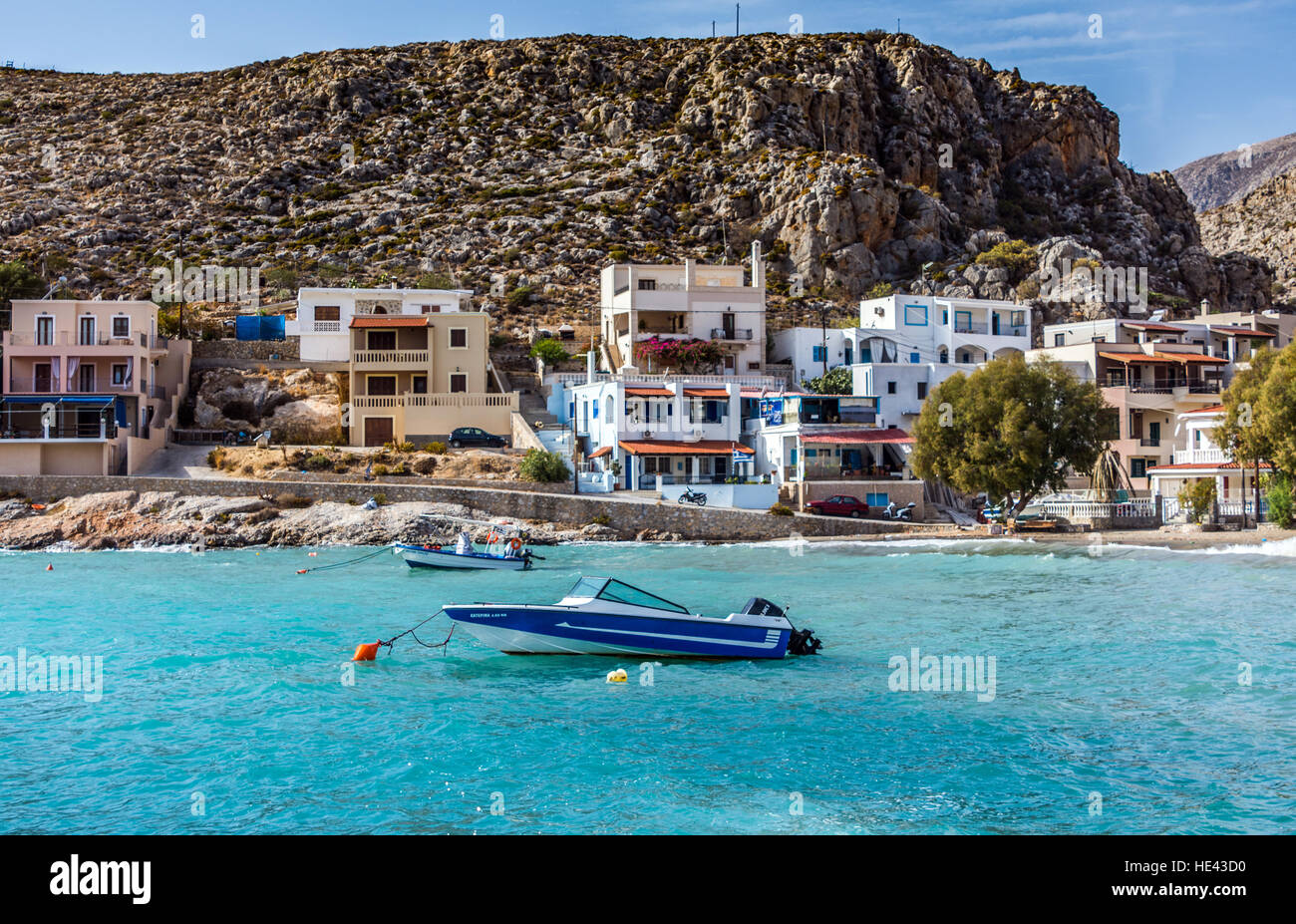 Pequeña lancha en mar azul aguamarina con casas que rodean la bahía de estilo griego Foto de stock