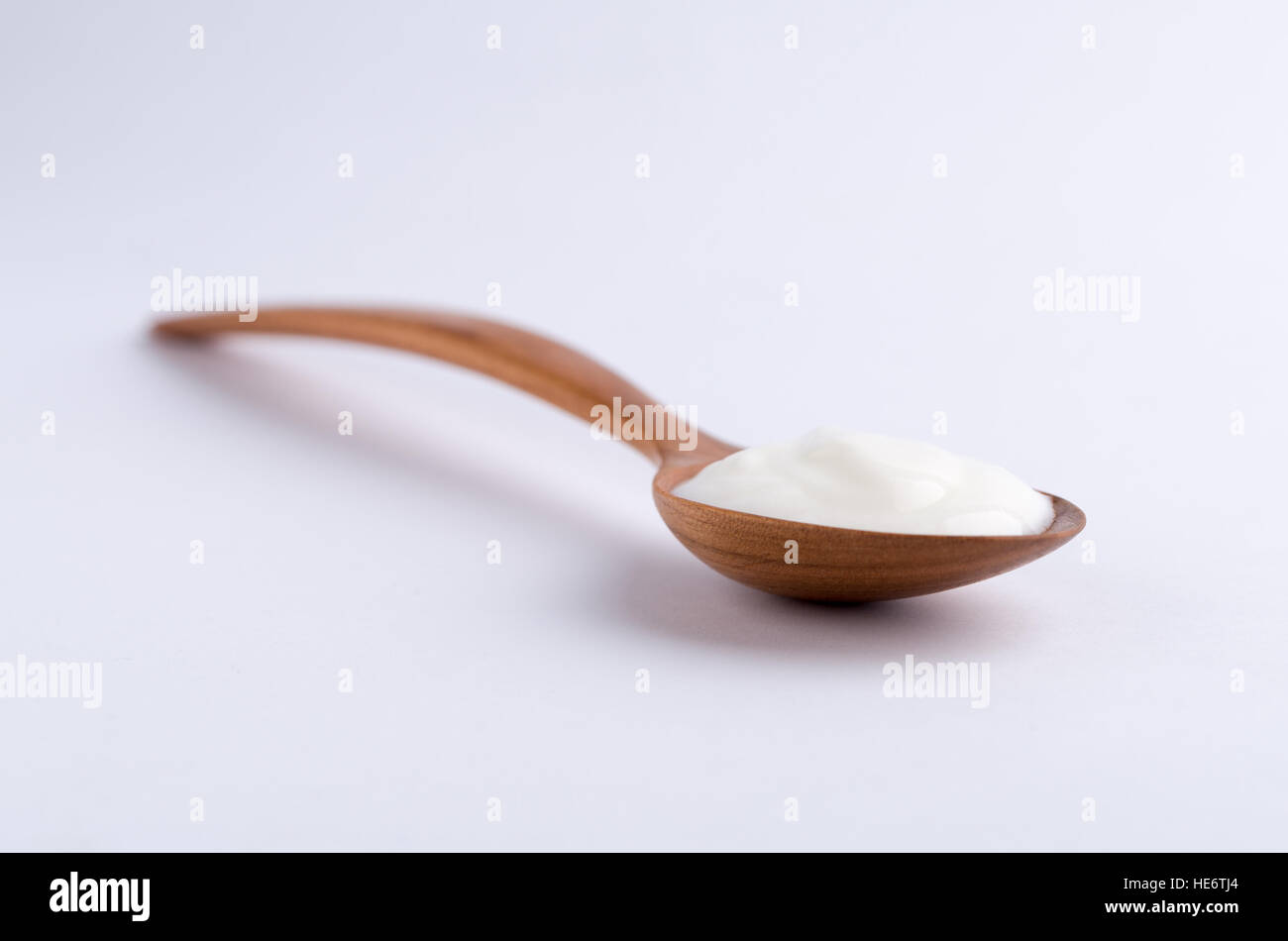 Cuchara de madera llena de yogur blanco sobre fondo blanco. Foto de stock