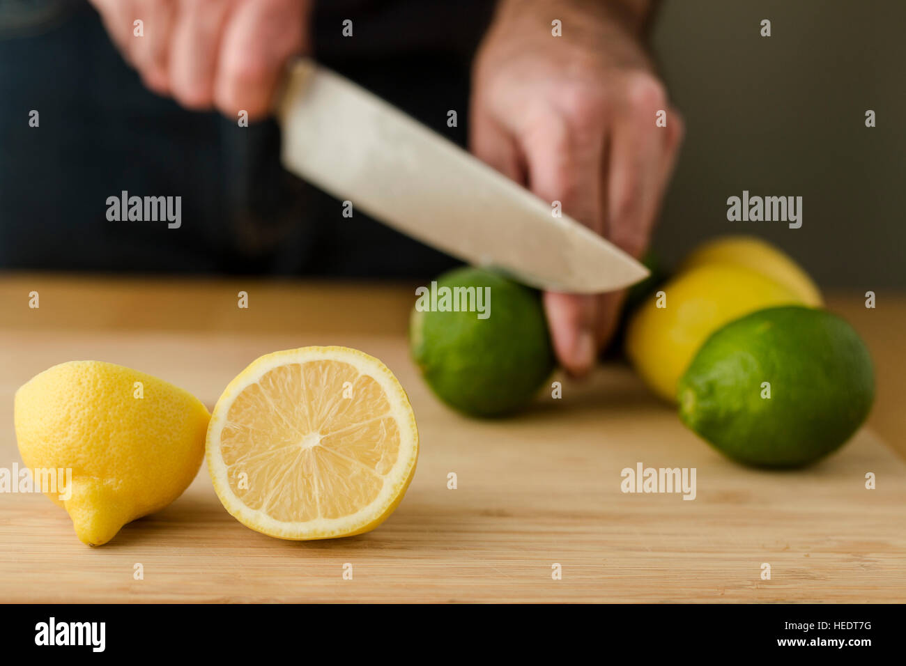 Un hombre de manos trocear los limones y limas en una tabla para cortar con un cuchillo del chef. Foto de stock