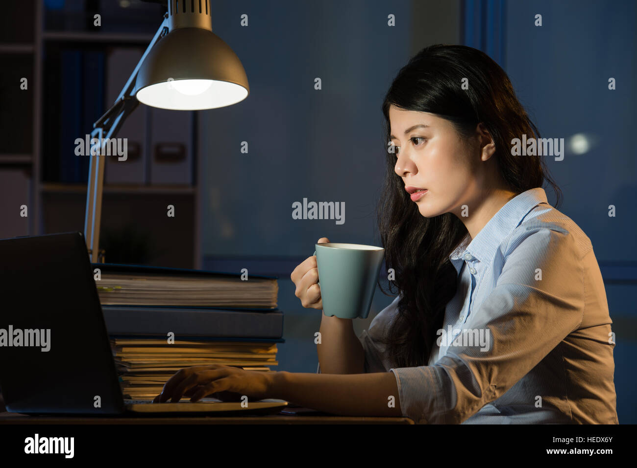 Mujer de negocios asiáticos beben café refrescante trabajando horas extraordinarias nocturnas interiores oficina de fondo. Foto de stock