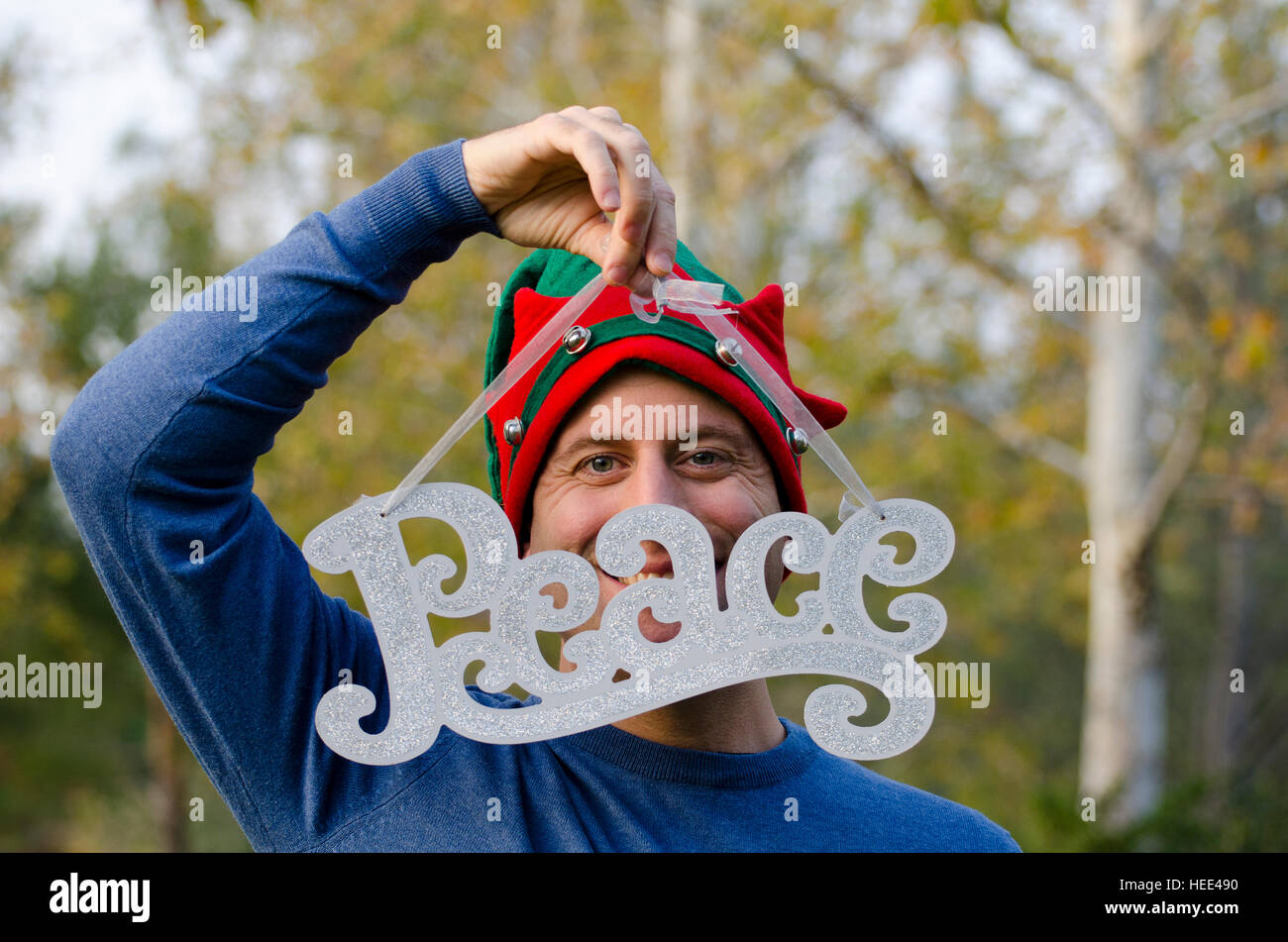 La paz en Navidad - Hombre escondiéndose detrás de la palabra paz vistiendo un sombrero de Navidad. Foto de stock