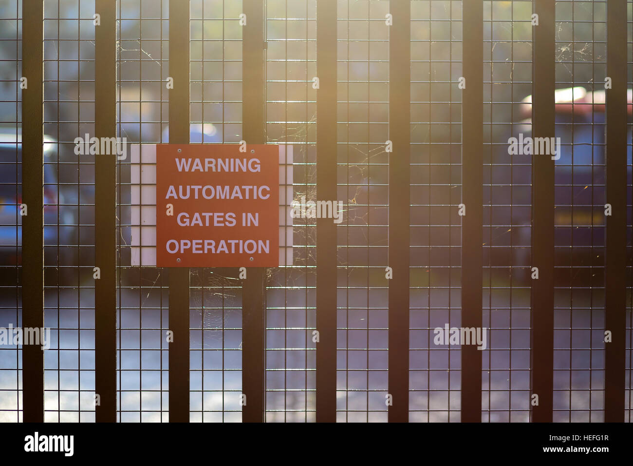 Advertencia puertas automáticas en operación, signo rojo sobre metal gate, lugar soleado. Foto de stock