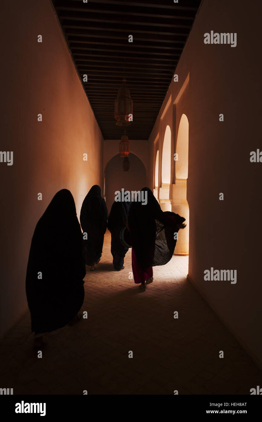 No identificados vestidos tradicionalmente a las mujeres locales caminatas en un pasillo oscuro de un palacio histórico en Ouarzazate Foto de stock