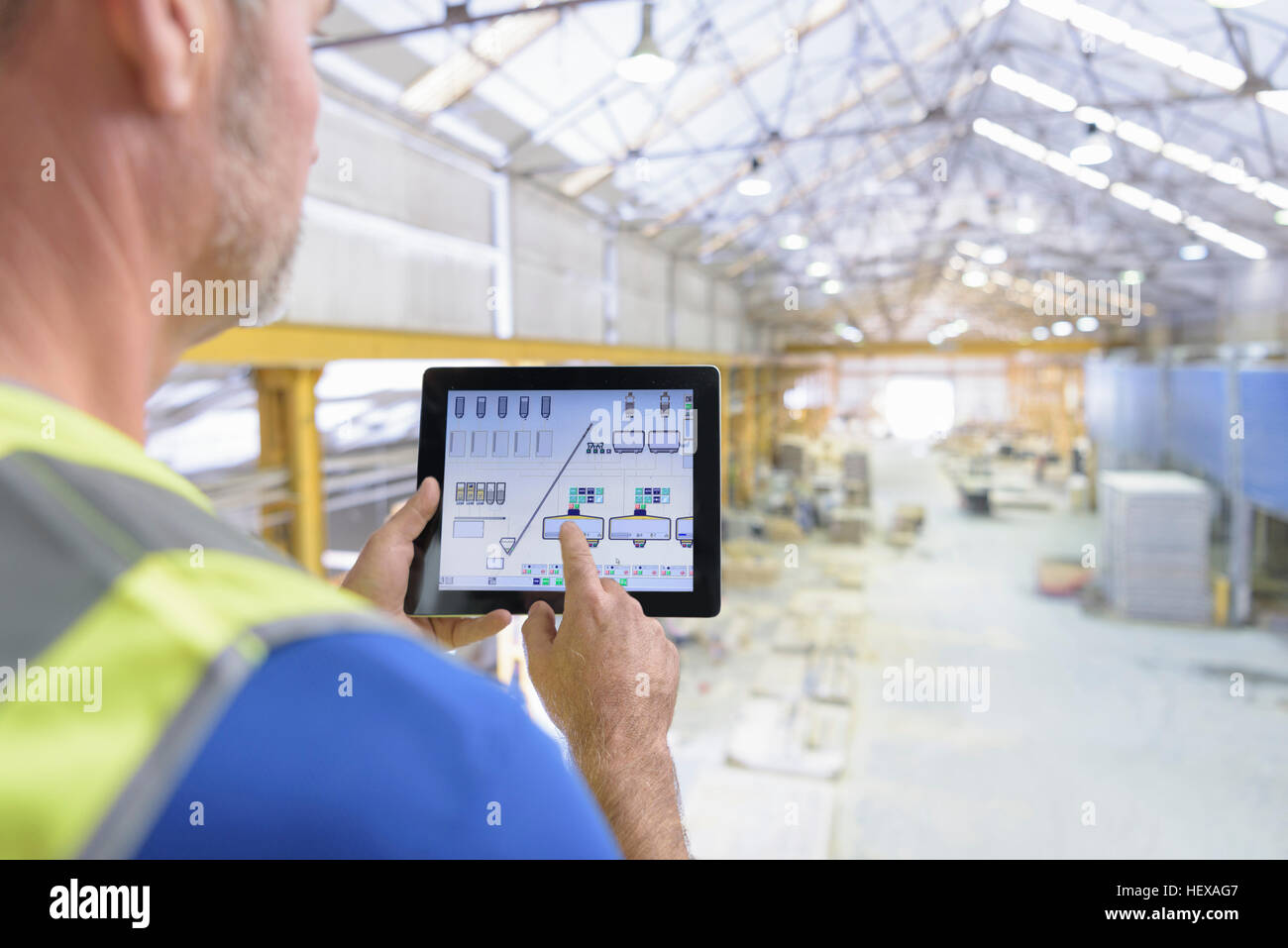 Trabajador utilizando tablet digital para controlar el mecanismo robótico en fábrica de piedra arquitectónica Foto de stock