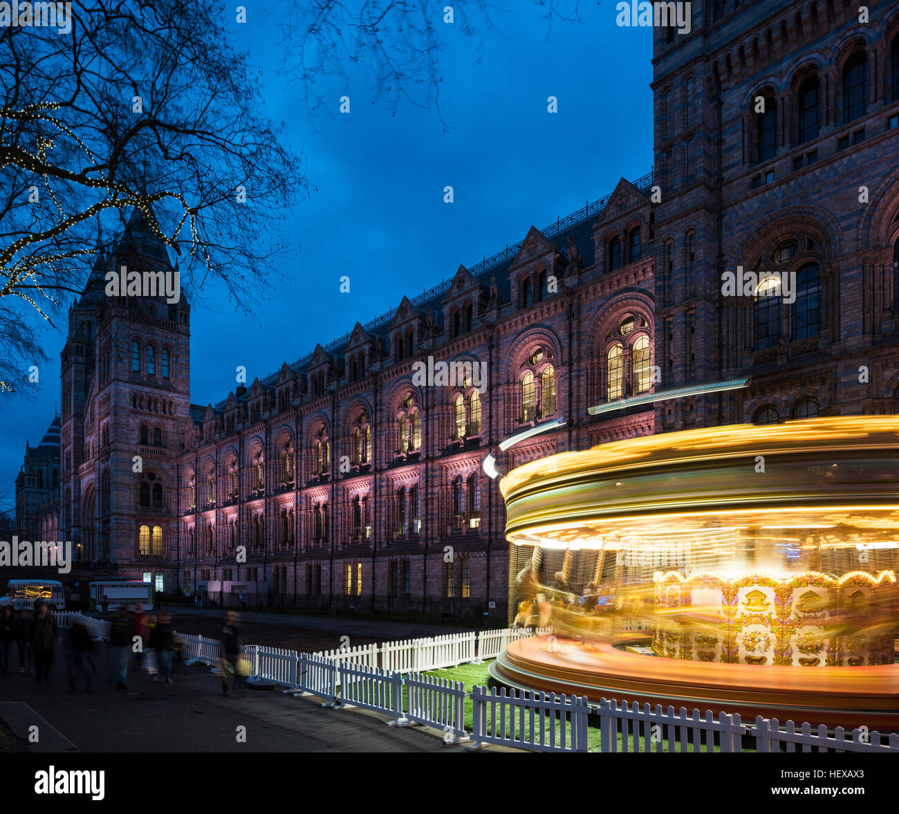 Carrusel gira iluminada por el Museo de Historia Natural en el crepúsculo, Londres, Reino Unido. Foto de stock