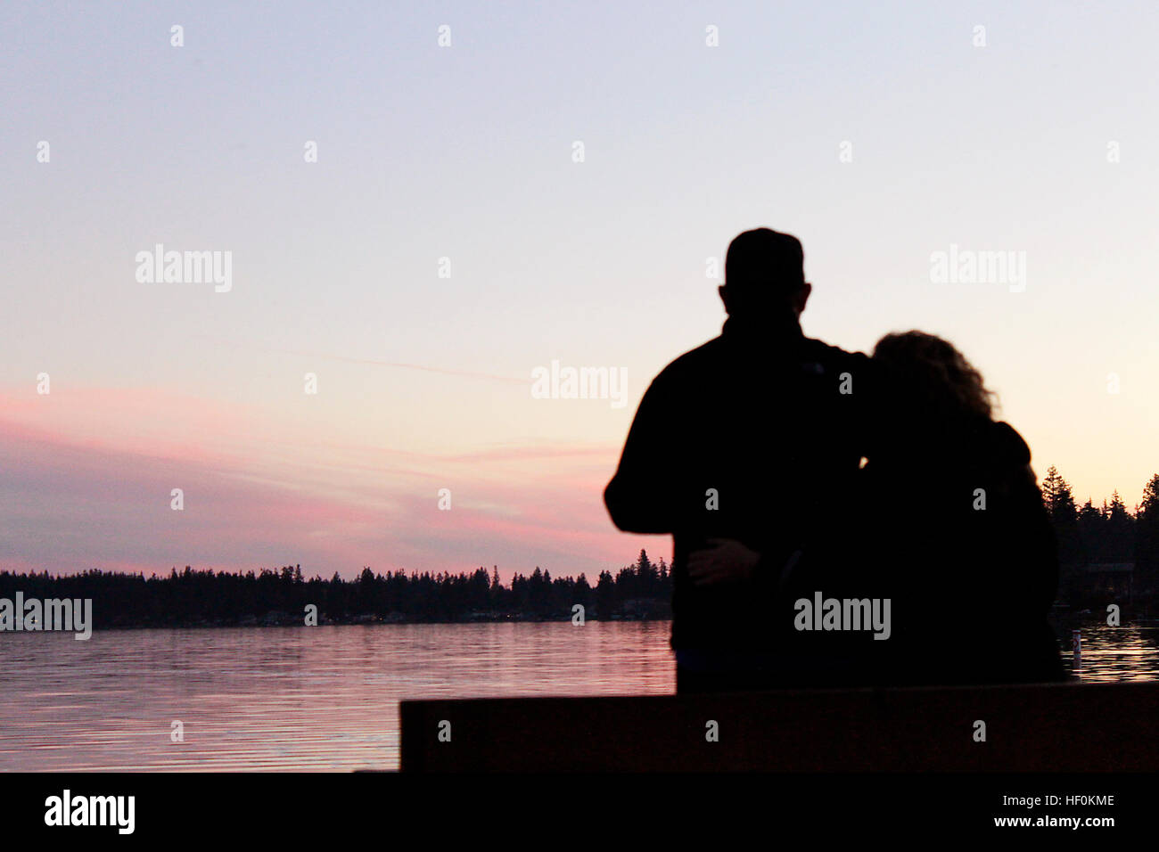 Silueta de una pareja inclinada contra las otras con vistas a la puesta de sol sobre el lago. Foto de stock