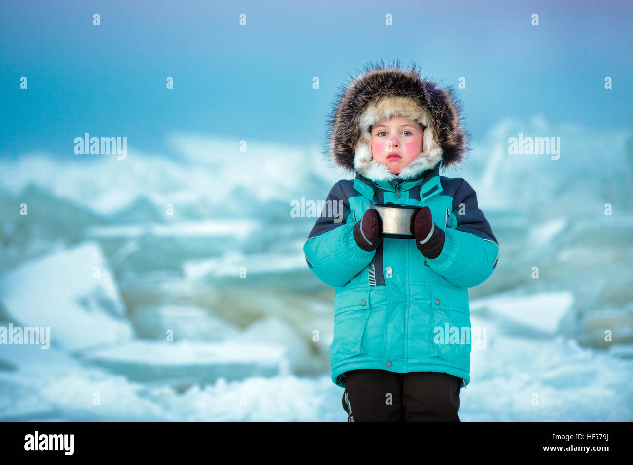 Cinco años muchacho lindo bebiendo té caliente en invierno mar congelado Foto de stock