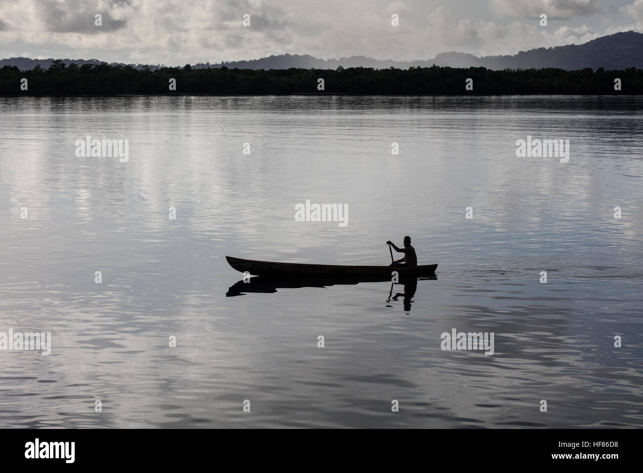 Las palas de un pescador su canoa en aguas tranquilas entre las islas remotas, en las Islas Salomón. Foto de stock