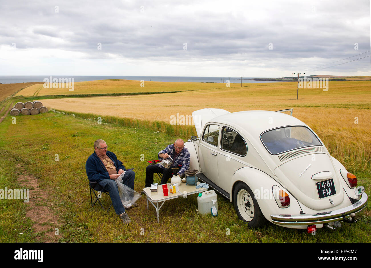 Dos holandeses tienen un picnic junto a sus VW beetle en un campo cerca de St Abbs, Berwickshire, Scottish Borders, Scotland, Reino Unido Foto de stock