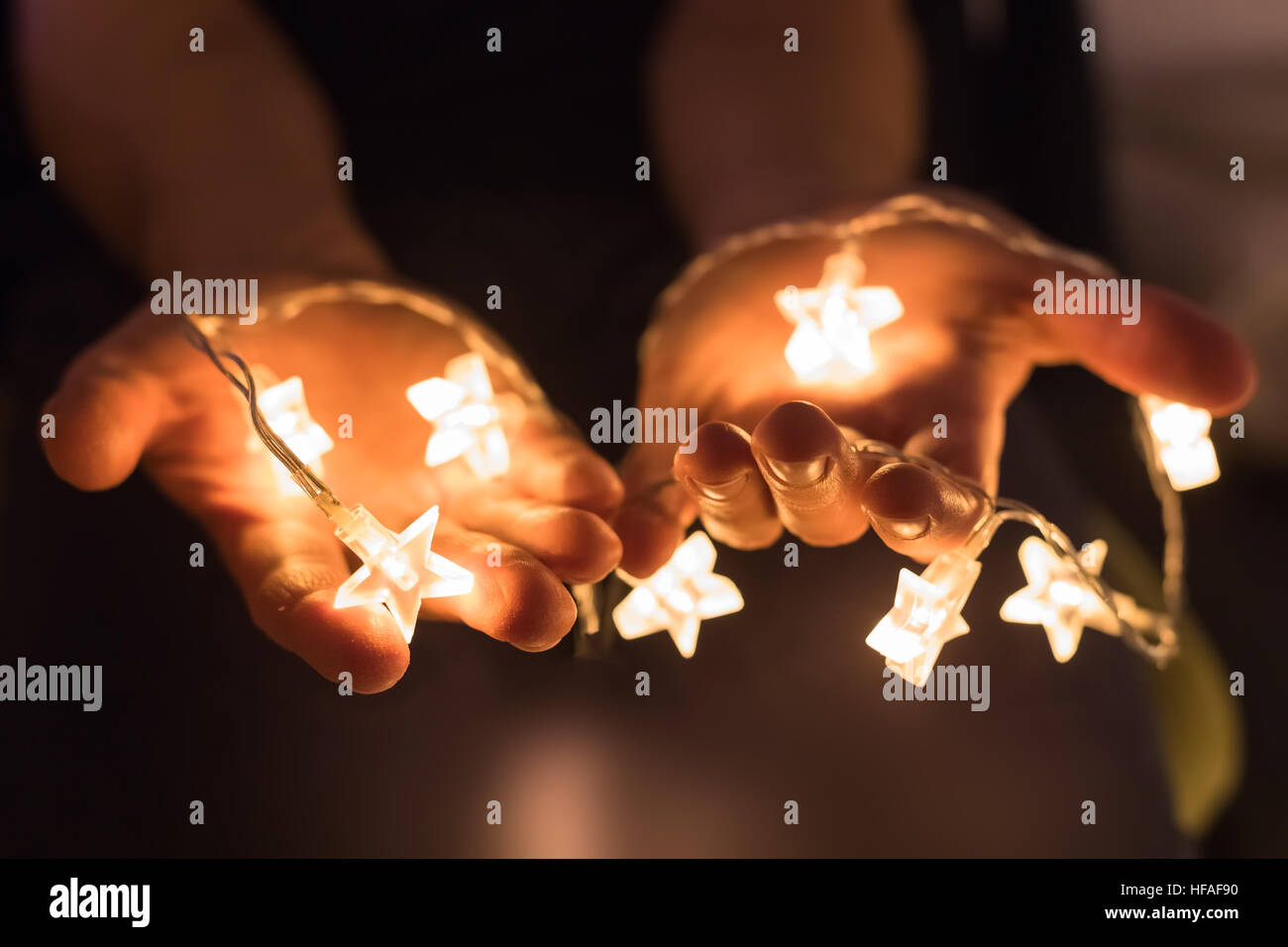 Manos sosteniendo brillantes luces de Navidad con formas de estrella Foto de stock