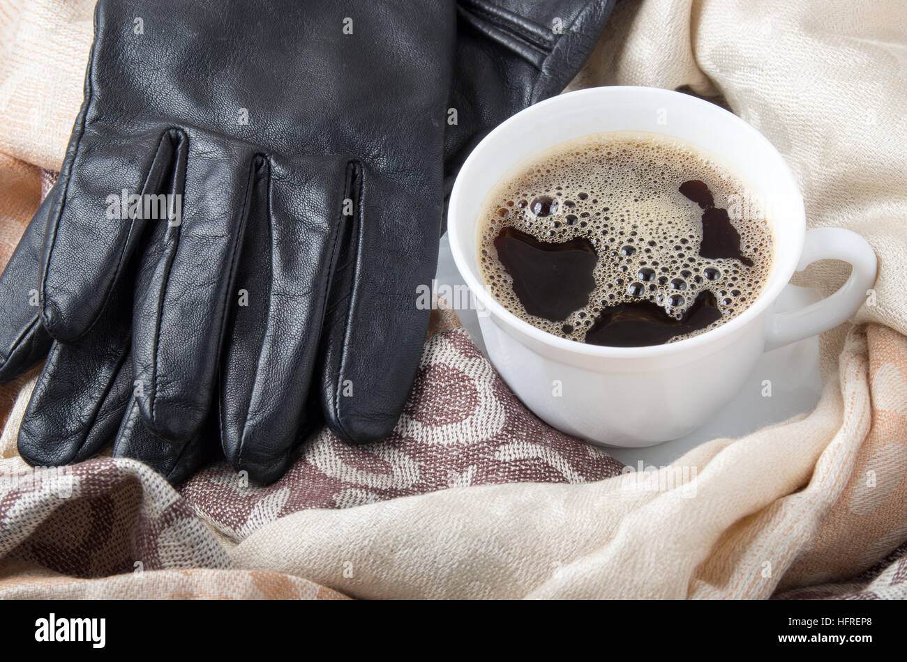 Ver de cerca en una taza de café blanco en los pliegues de la hembra de bufanda y guantes de cuero negro. Foto de stock
