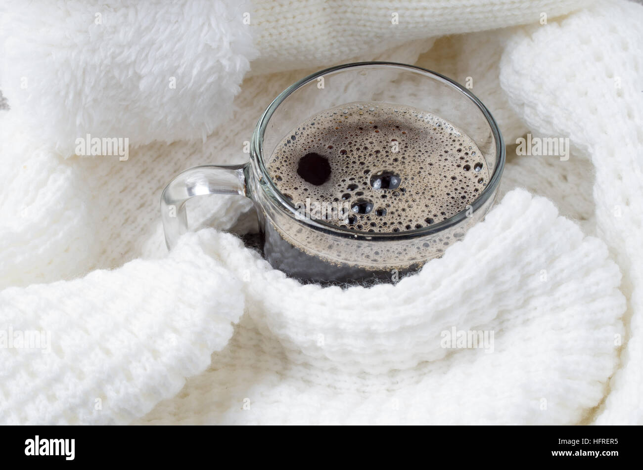 Jarra de cristal transparente con café caliente cerca envuelto en una bufanda de lana blanca con poca profundidad de foco. Foto de stock
