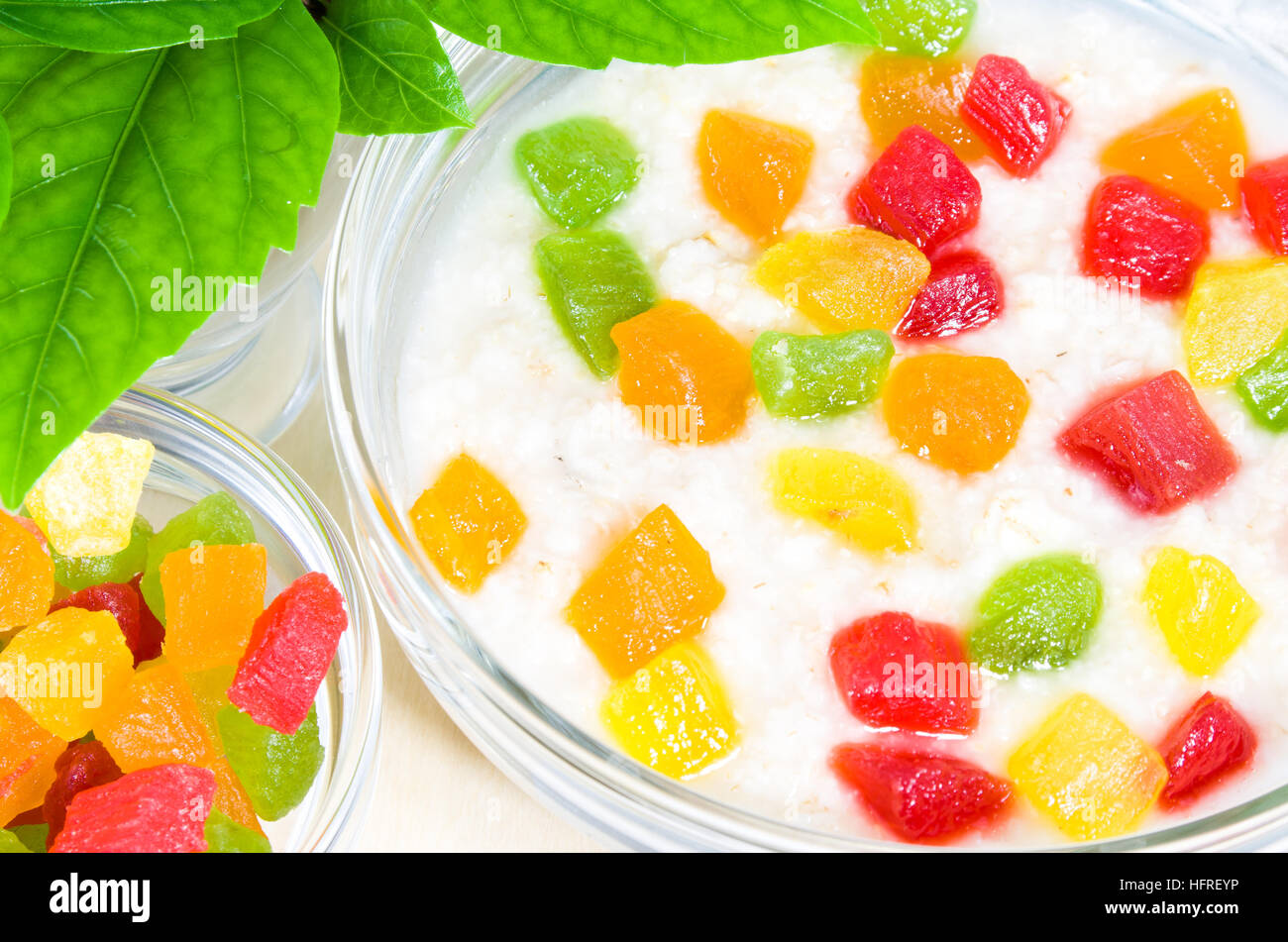 Tazón de vidrio con avena saludables de cerca con coloridas frutas confitadas para desayunar está iluminado por la luz solar desde la ventana Foto de stock