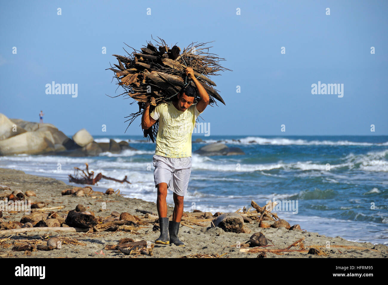 El hombre lleva el paquete de madera sobre la playa, el Parque Nacional Tayrona, entre el Caribe y la Sierra Nevada de Santa Marta, Colombia. Foto de stock