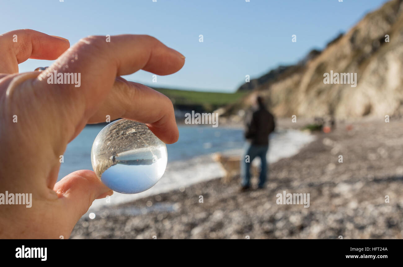 Mirando a través de una bola de cristal para el hombre y el perro en la playa en día soleado Foto de stock