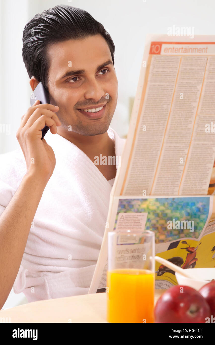 Hombre hablando por teléfono y leyendo un periódico a la mesa de desayuno Foto de stock