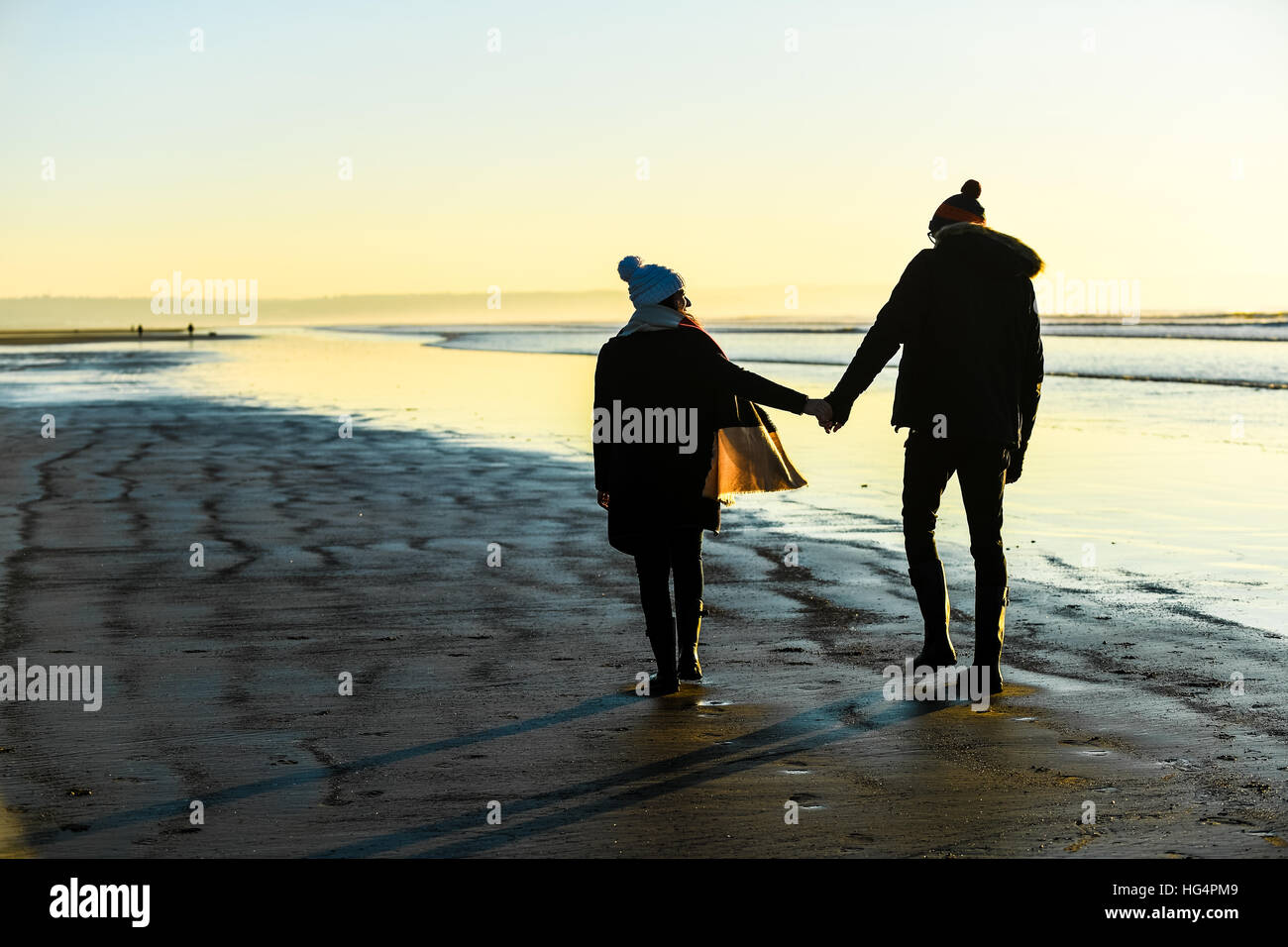 Una pareja de jóvenes enamorados tomados de la mano en una playa al atardecer. Foto de stock