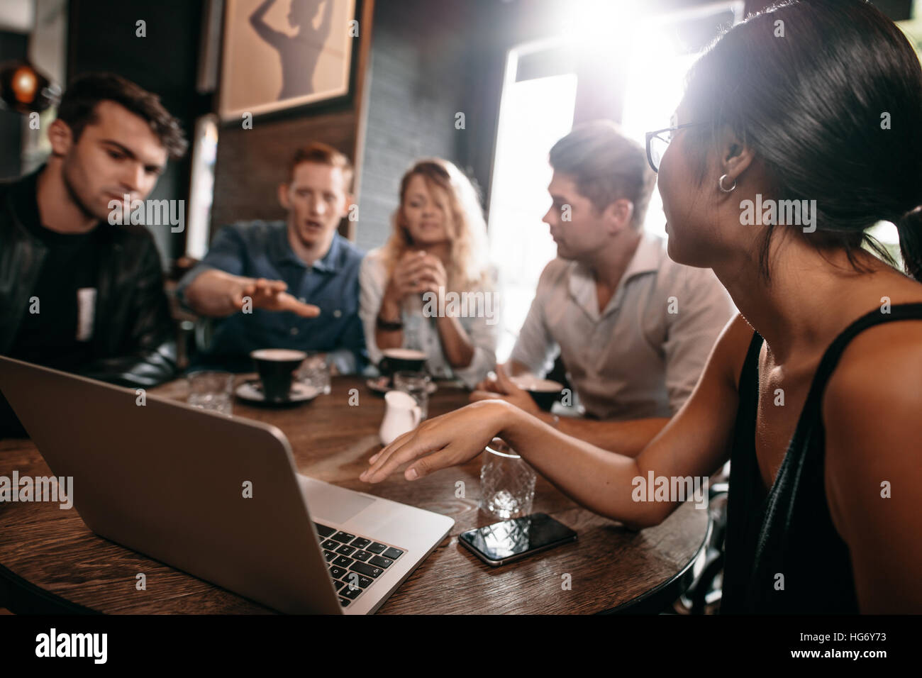 Jóvenes amigos mirando un portátil en cafe y discutiendo. Los jóvenes con un portátil en la cafetería. Foto de stock
