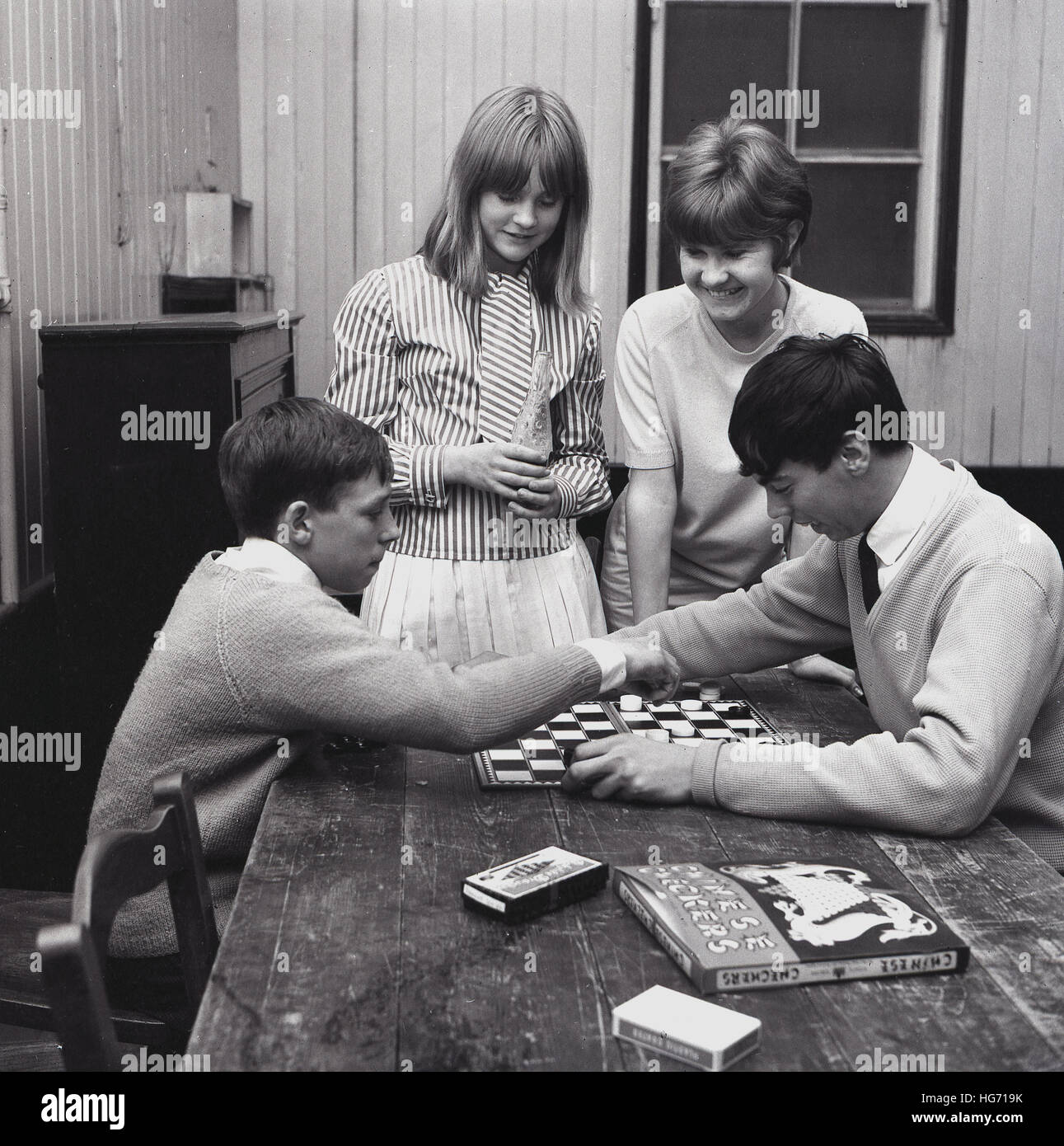 1960, históricos, dos niños sentados en una mesa, con dos chicas que buscan  en inglés, jugar 'borradores', un juego de tablero de estrategia, con otro  juego de mesa, "damas chinas" sobre la