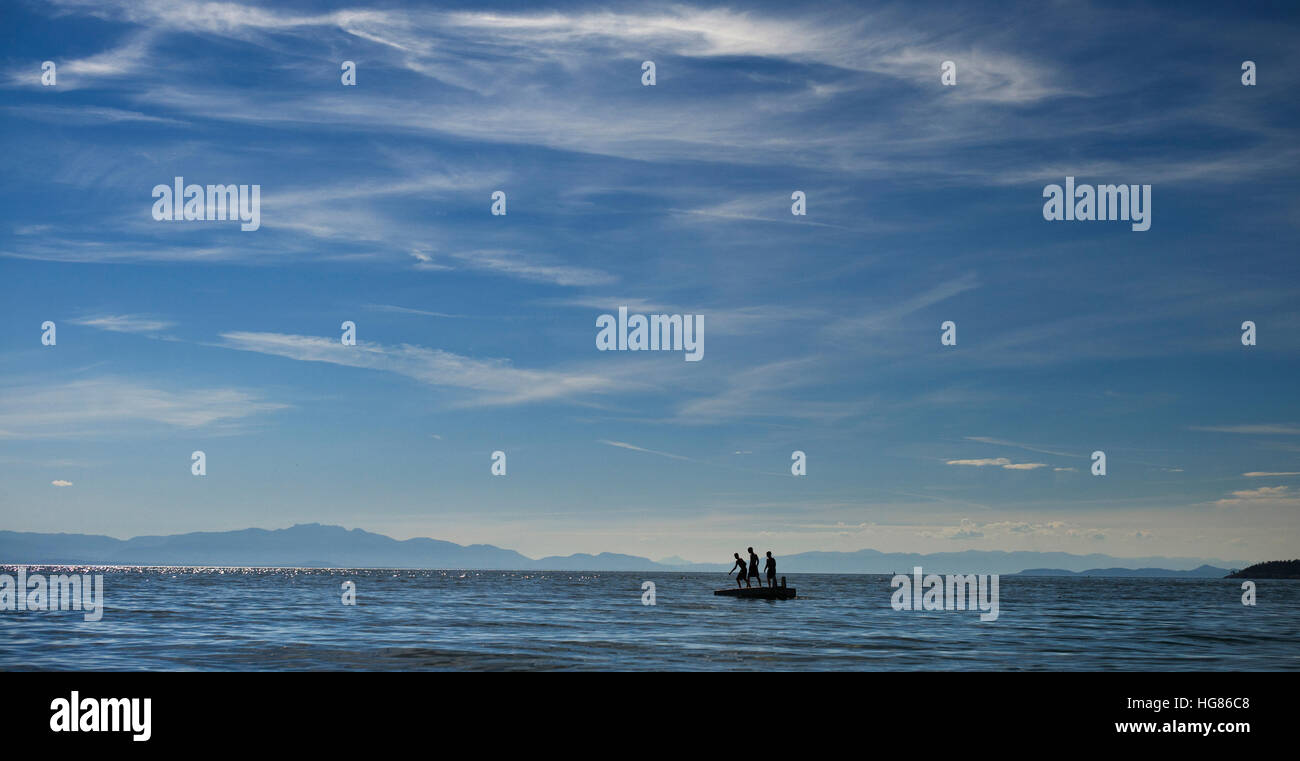 Silueta gente de pie en la plataforma flotante en el mar contra el cielo Foto de stock