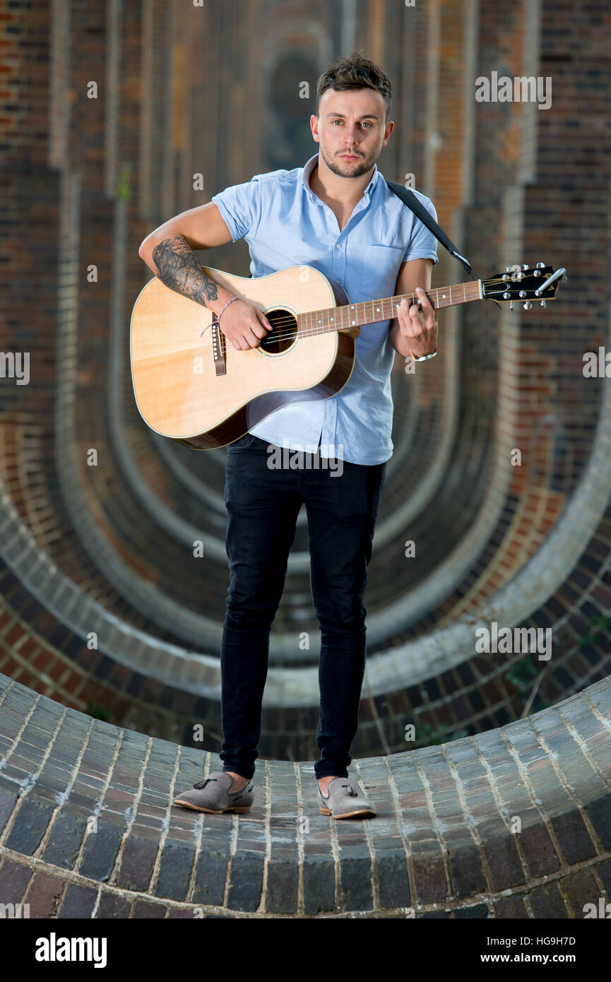 Cantante, compositor Jamie Mathias posa con su guitarra para un rodaje en el Ouse valle del viaducto, Sussex, Reino Unido. Foto de stock