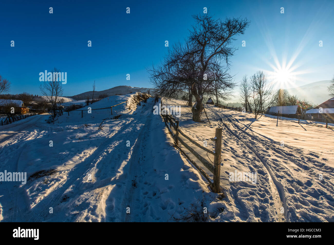 Valla en el ámbito rural cubierto de nieve en la ladera de montaña cerca de la aldea de día de invierno Foto de stock