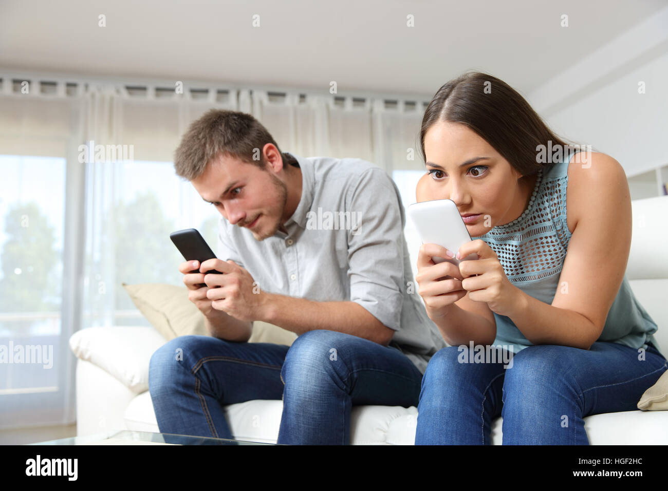 Obsesionado par de acompañantes con sus teléfonos inteligentes ignorarse mutuamente sentados en un sofá en casa Foto de stock