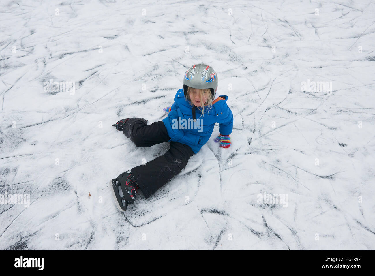 Adorable pequeño niño niña patinaje sobre hielo en invierno, la nieve día al aire libre en el parque el estanque congelado. Llevar un casco de seguridad Foto de stock