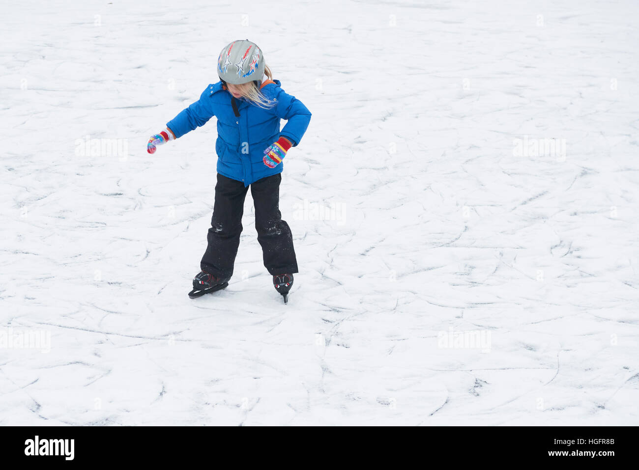 Adorable pequeño niño niña patinaje sobre hielo en invierno, la nieve día al aire libre en el parque el estanque congelado. Llevar un casco de seguridad Foto de stock