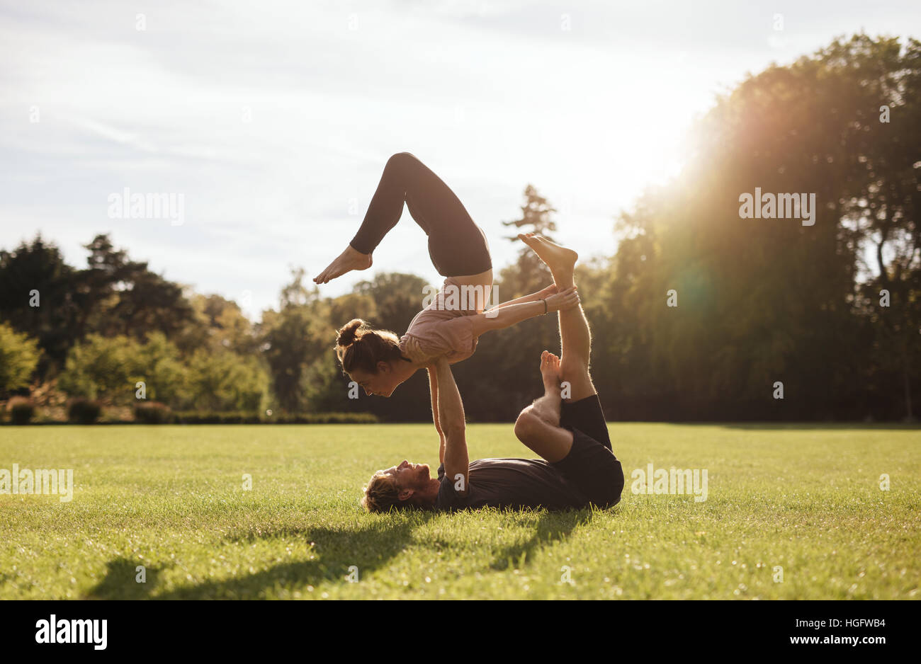 Colocar pareja realizando ejercicios de yoga acrobático en el parque. Hombre tumbado sobre el césped y equilibrar la mujer al aire libre. Foto de stock