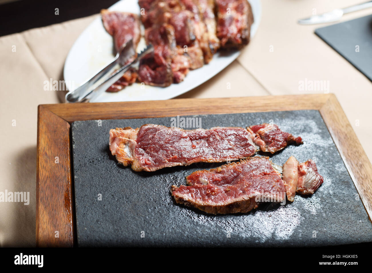 Corte el bistec de carne en una placa blanca y placa caliente shot con luz artificial. Foto de stock